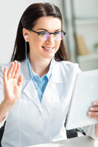 Atractivo médico sonriente en los auriculares que tienen consulta en línea en la tableta digital en la oficina - foto de stock