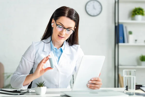 Positive doctor showing pills to patient on online consultation on digital tablet in clinic office — Stock Photo