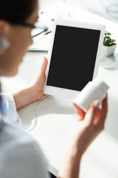 Cropped view of doctor holding pills while having online consultation on digital tablet with blank screen — Stock Photo