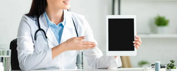 Plano panorámico del médico sonriente mostrando tableta digital con pantalla en blanco en la oficina de la clínica - foto de stock