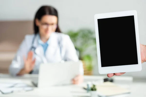 Cropped view of man holding digital tablet with blank screen in clinic office with doctor having online consultation on laptop, selective focus — Stock Photo