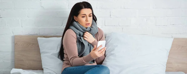 Панорамний знімок привабливої хворої жінки з грипом, що має онлайн-консультацію з лікарем на смартфоні — стокове фото