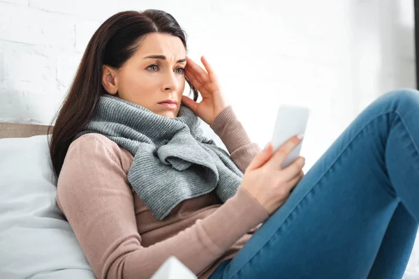 Усталая больная женщина с головной болью, имеющая онлайн консультации с врачом на смартфоне — стоковое фото