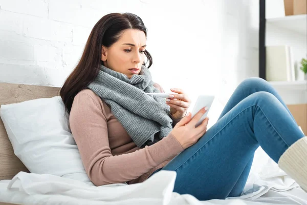 Femme malade avec thermomètre ayant une consultation en ligne avec un médecin sur smartphone — Photo de stock