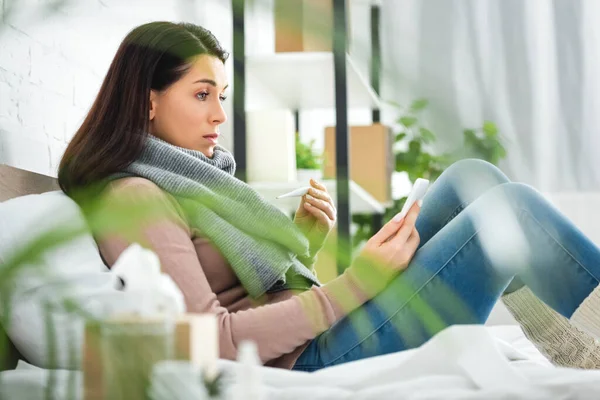 Sick woman with thermometer having online consultation with doctor on smartphone — Stock Photo