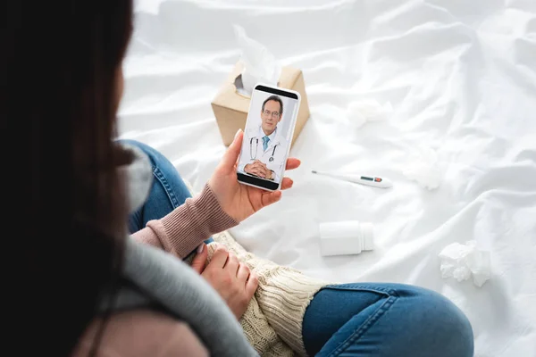 Vista recortada de la mujer enferma con pastillas y termómetro que tiene consulta en línea con el médico masculino en el teléfono inteligente - foto de stock