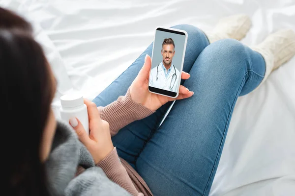 Vista recortada de la mujer enferma con píldoras que tienen consulta en línea con el médico masculino en el teléfono inteligente - foto de stock