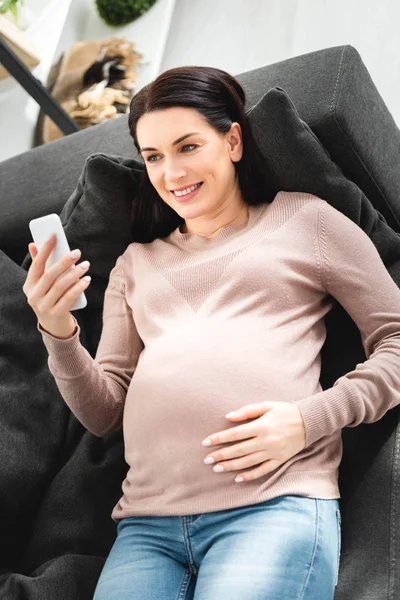 Mujer embarazada positiva que tiene consulta en línea con el médico en el teléfono inteligente - foto de stock