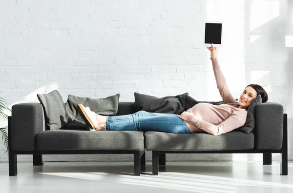 Улыбающаяся беременная женщина, держащая цифровой планшет с чистым экраном, лежа на диване — стоковое фото
