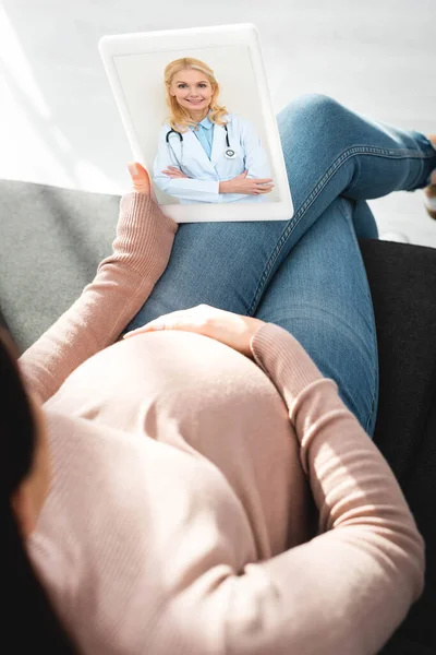 Vue recadrée de la femme enceinte ayant consultation en ligne avec le médecin féminin sur tablette numérique à la maison — Photo de stock