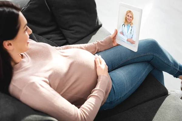 Atractiva mujer embarazada que tiene consulta en línea con el médico femenino en la tableta digital - foto de stock