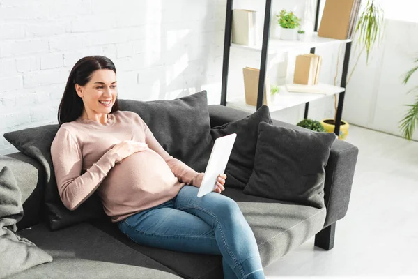 Mujer embarazada que tiene consulta en línea con el médico en tableta digital en casa - foto de stock