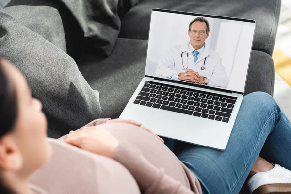 Geschnittene Ansicht einer schwangeren Patientin mit Online-Konsultation mit dem Arzt auf dem Laptop — Stockfoto