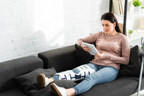 Красивая женщина со сломанной ногой, имеющая онлайн консультацию с врачом на цифровом планшете дома — стоковое фото