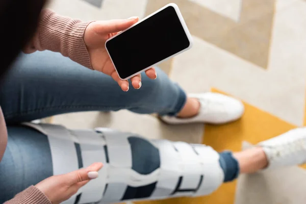 Vue recadrée de la femme avec attelle de jambe ayant consultation en ligne avec le médecin sur smartphone avec écran blanc — Photo de stock