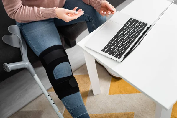 Visão cortada da mulher com a perna quebrada ter consulta on-line com o médico no laptop em casa — Fotografia de Stock