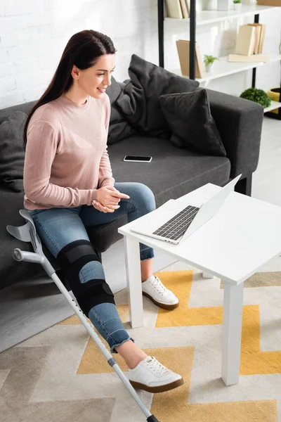 Приваблива жінка з розбитою ногою, що має онлайн-консультацію лікаря на ноутбуці вдома — стокове фото