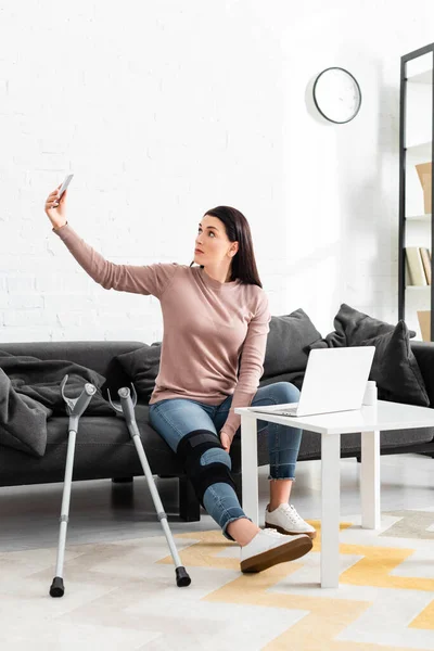 Femme avec jambe cassée ayant une consultation en ligne avec un médecin sur ordinateur portable et smartphone — Photo de stock