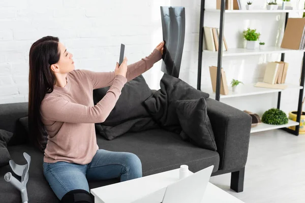 Woman taking photo of leg x-ray for online consultation with doctor on laptop — Stock Photo