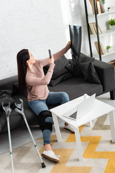 Woman taking photo of leg x-ray for online consultation with doctor on laptop — Stock Photo