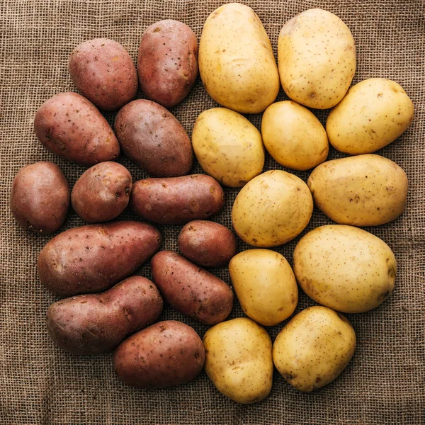 Vue du dessus des pommes de terre crues biologiques disposées en cercle sur un sac rustique brun — Photo de stock
