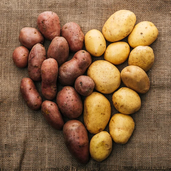 Vista superior de patatas crudas orgánicas dispuestas en el corazón en saco rústico marrón - foto de stock
