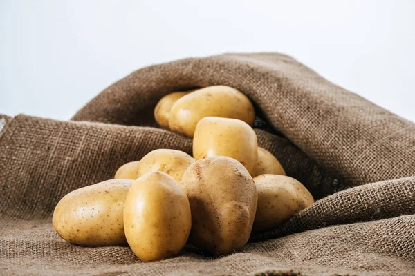 Patatas crudas orgánicas en saco rústico marrón aislado en blanco - foto de stock