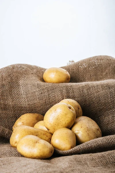 Batatas cruas orgânicas em pano de saco rústico marrom isolado em branco — Fotografia de Stock