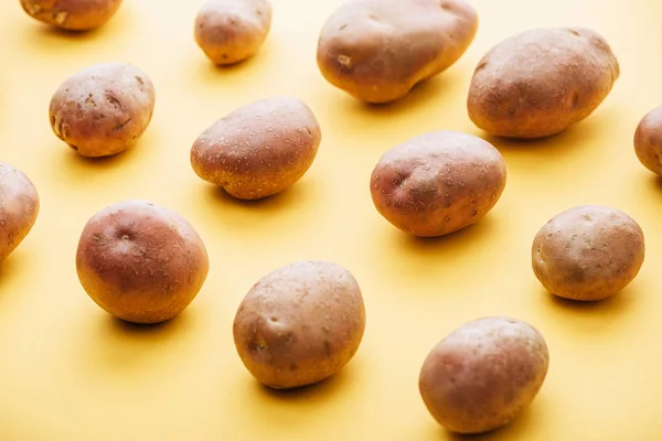 Pattern of raw whole fresh potatoes on yellow background — Stock Photo