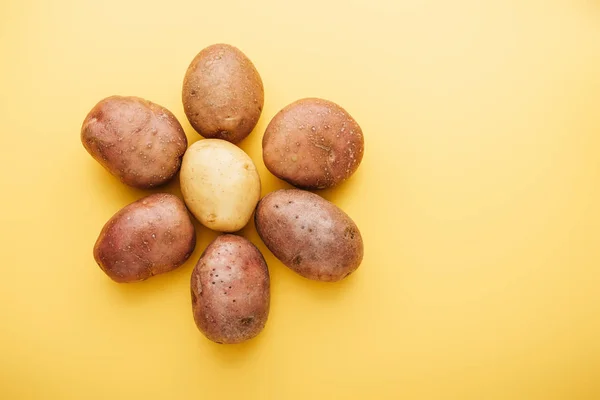 Vista superior de batatas frescas inteiras cruas dispostas em flor sobre fundo amarelo — Fotografia de Stock