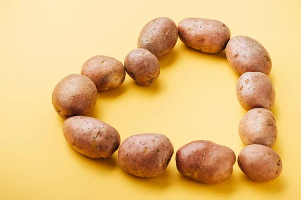 Rohe ganze frische Kartoffeln im Herzen auf gelbem Hintergrund angeordnet — Stockfoto