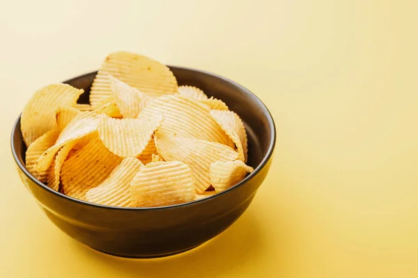 Deliciosas batatas fritas crocantes na tigela no fundo amarelo — Fotografia de Stock