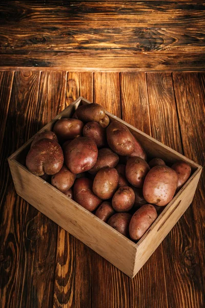 Fresh ripe potatoes in box on wooden background — Stock Photo