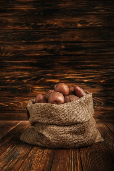 Ripe potatoes in rustic sack on wooden background — Stock Photo