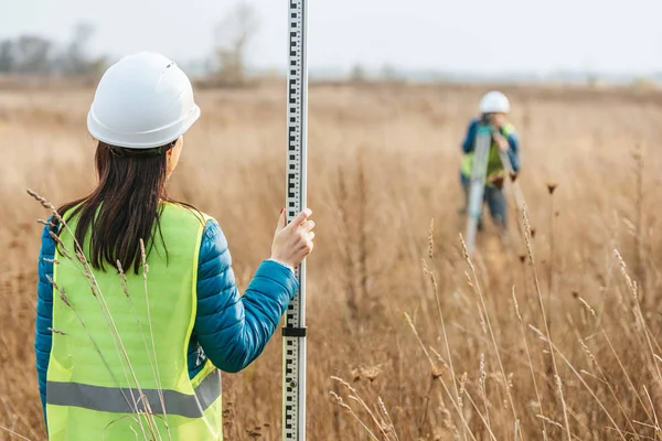 Selective focus of surveyors with survey ruler and digital level in field — Stock Photo