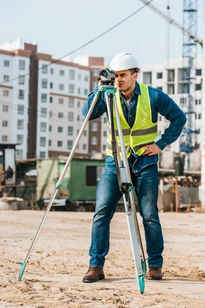 Surveyor in hardhat e giacca ad alta visibilità con livello digitale in cantiere — Foto stock