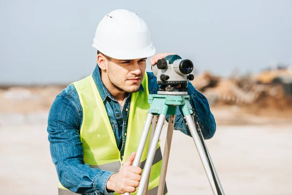 Сервеєр у куртці Hardhat та високої видимості, який дивиться на цифровому рівні — стокове фото