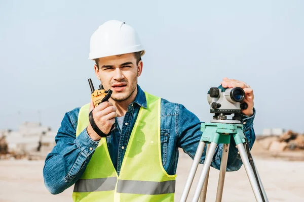 Gutaussehender Vermessungsingenieur mit digitalem Pegel, der am Radio spricht — Stockfoto