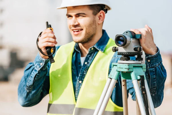 Enfoque selectivo del topógrafo que mantiene el nivel digital y habla por radio - foto de stock