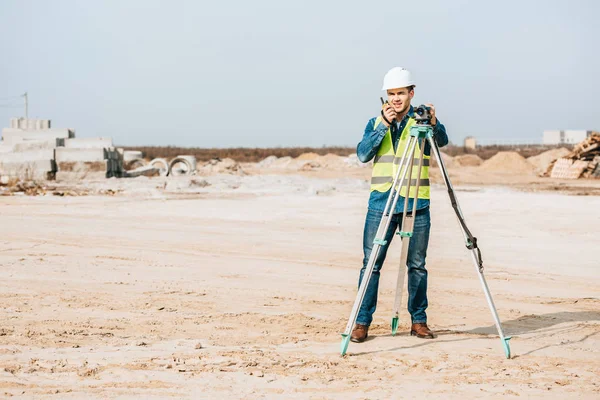 Surveyor with digital level talking on radio set on dirt road — Stock Photo