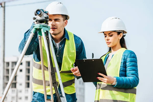 Vermessungsingenieur mit digitalem Pegel, während Kollege auf Klemmbrett schreibt — Stockfoto