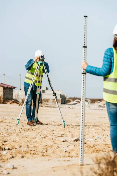 Selektiver Fokus der Vermessungsingenieure, die mit Lineal und digitaler Ebene auf der Baustelle arbeiten — Stockfoto