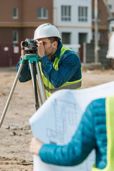 Selective focus of surveyors working with digital level and blueprint — Stock Photo