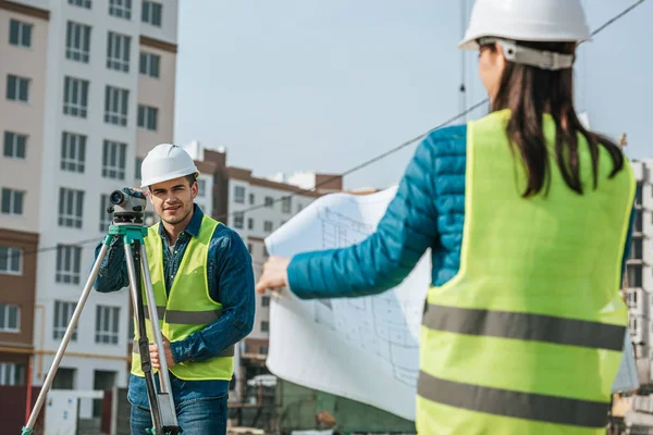 Selective focus of surveyor with digital level and colleague with blueprint — Stock Photo