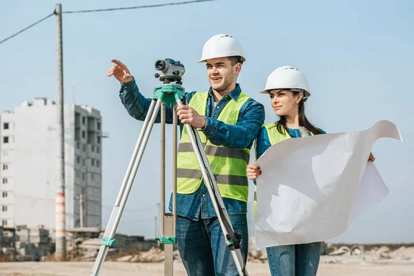Surveyor with digital level pointing away to colleague with blueprint — Stock Photo