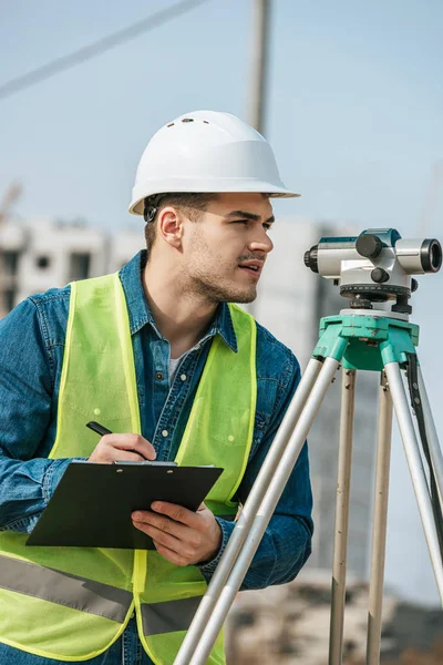 Surveyor with clipboard looking throughout digital level — Stock Photo