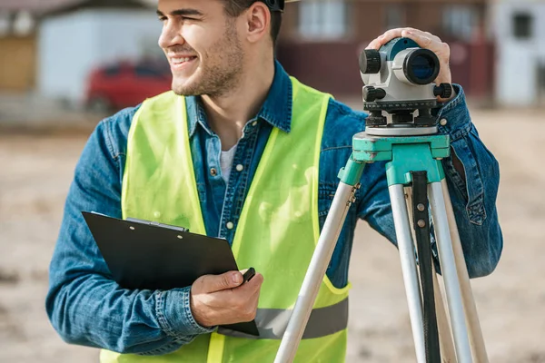 Smiling surveyor holding clipboard and digital level — Stock Photo