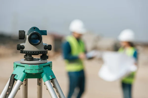 Selective focus of digital level and surveyors with blueprint at background — Stock Photo