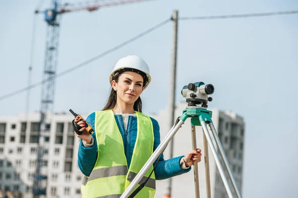 Sonriente topógrafo con nivel digital y radio en obra - foto de stock