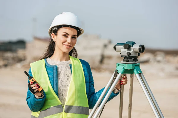 Atractivo topógrafo con nivel digital y radio sonriendo a la cámara - foto de stock